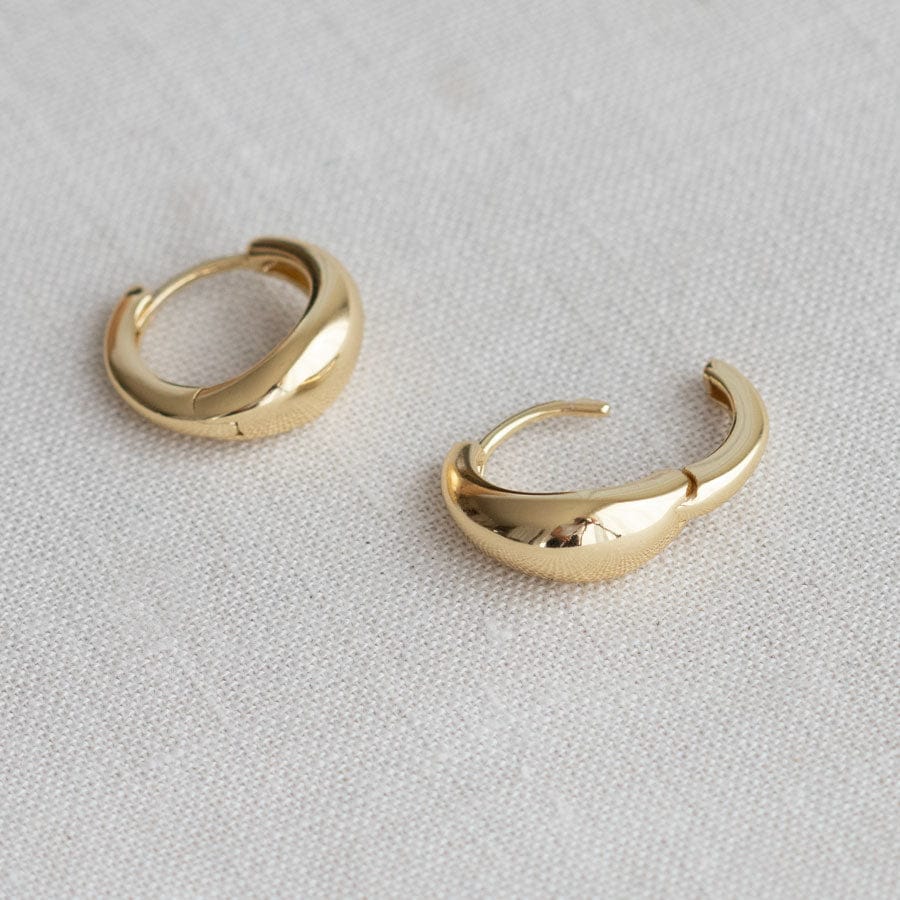 A pair of polished gold huggie hoop earrings resting on a textured off-white linen surface.